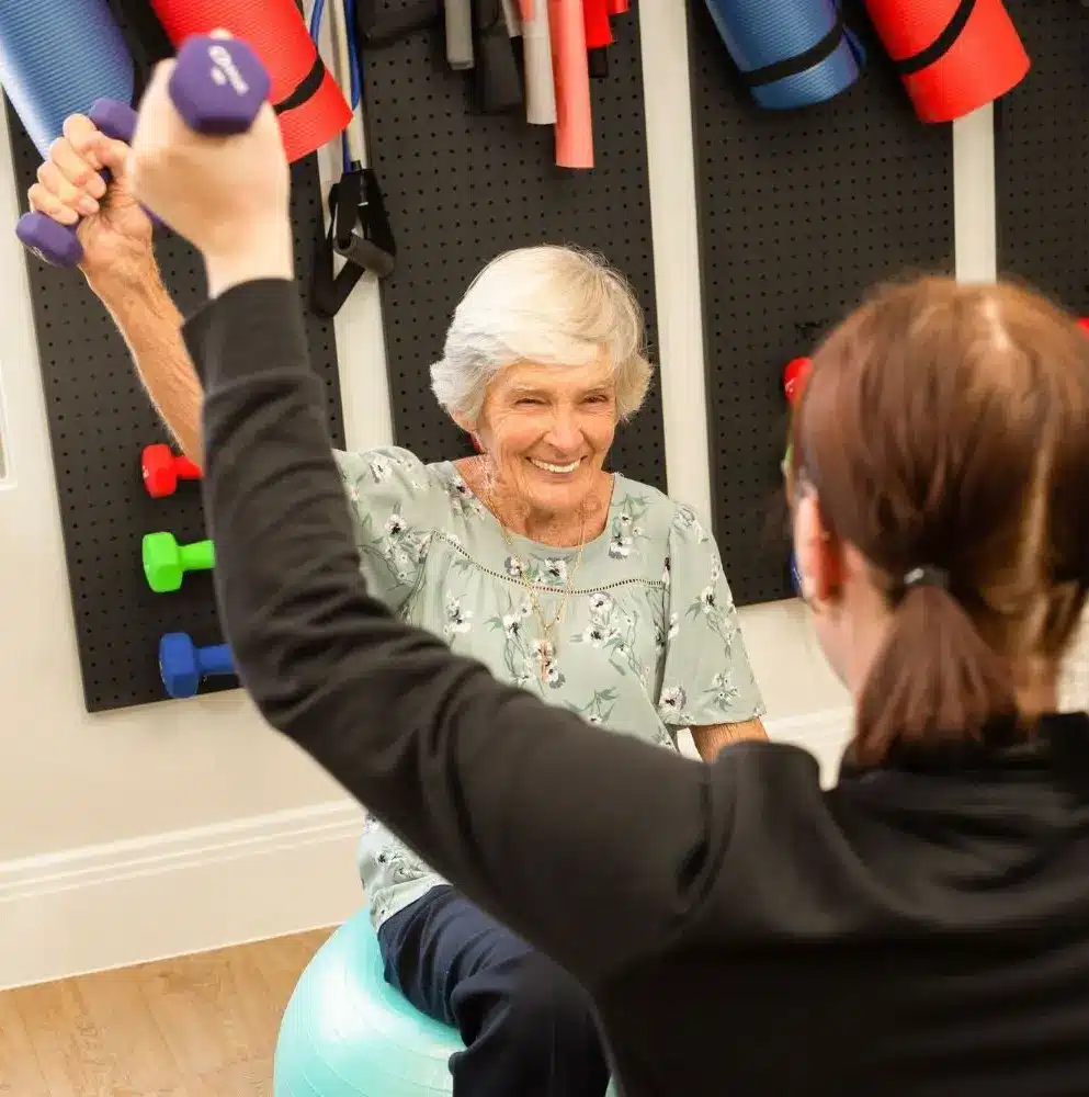 An old lady is exercising along with her trainer.