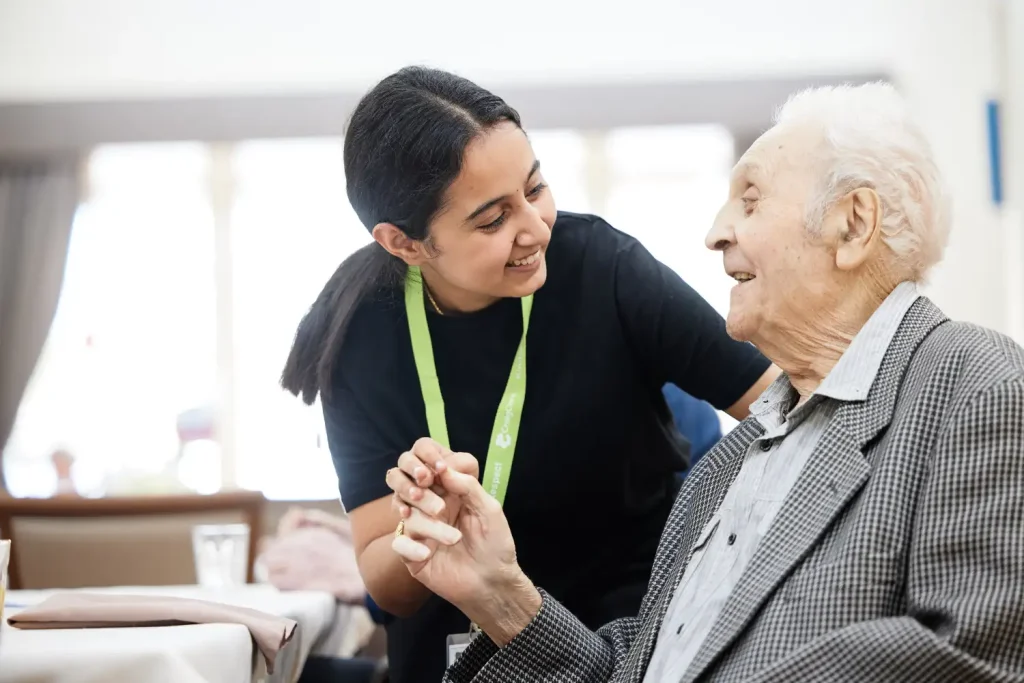 Aged care worker smiling and holding hands with an elderly man in a residential aged care hom